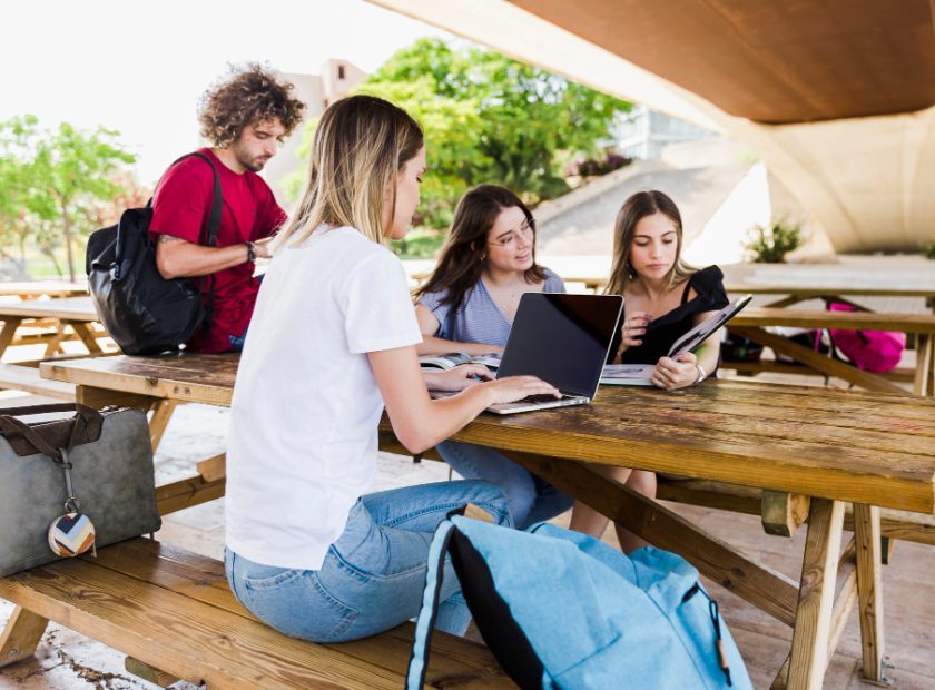 Estudiantes con portatiles en una mesa en el parque